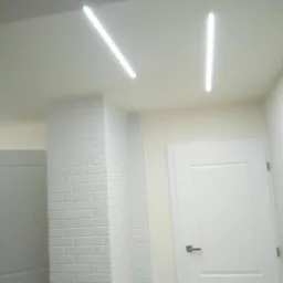 Białe wnętrze z kolumną obłożoną białą cegłą, oświetleniem LED na suficie i białą stolarką drzwiową.