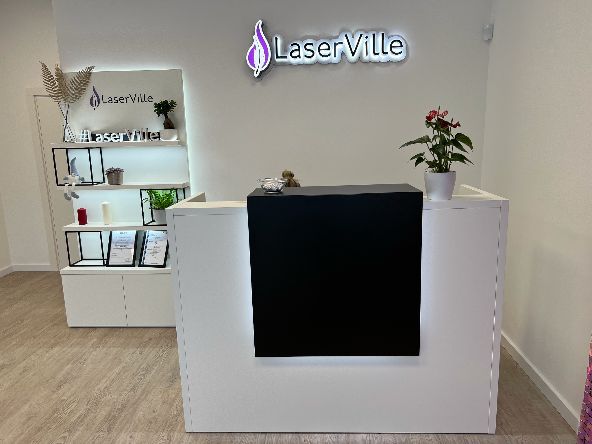 Recepcja w salonie kosmetycznym LaserVille z logo, roślinami i dekoracjami na półkach.
