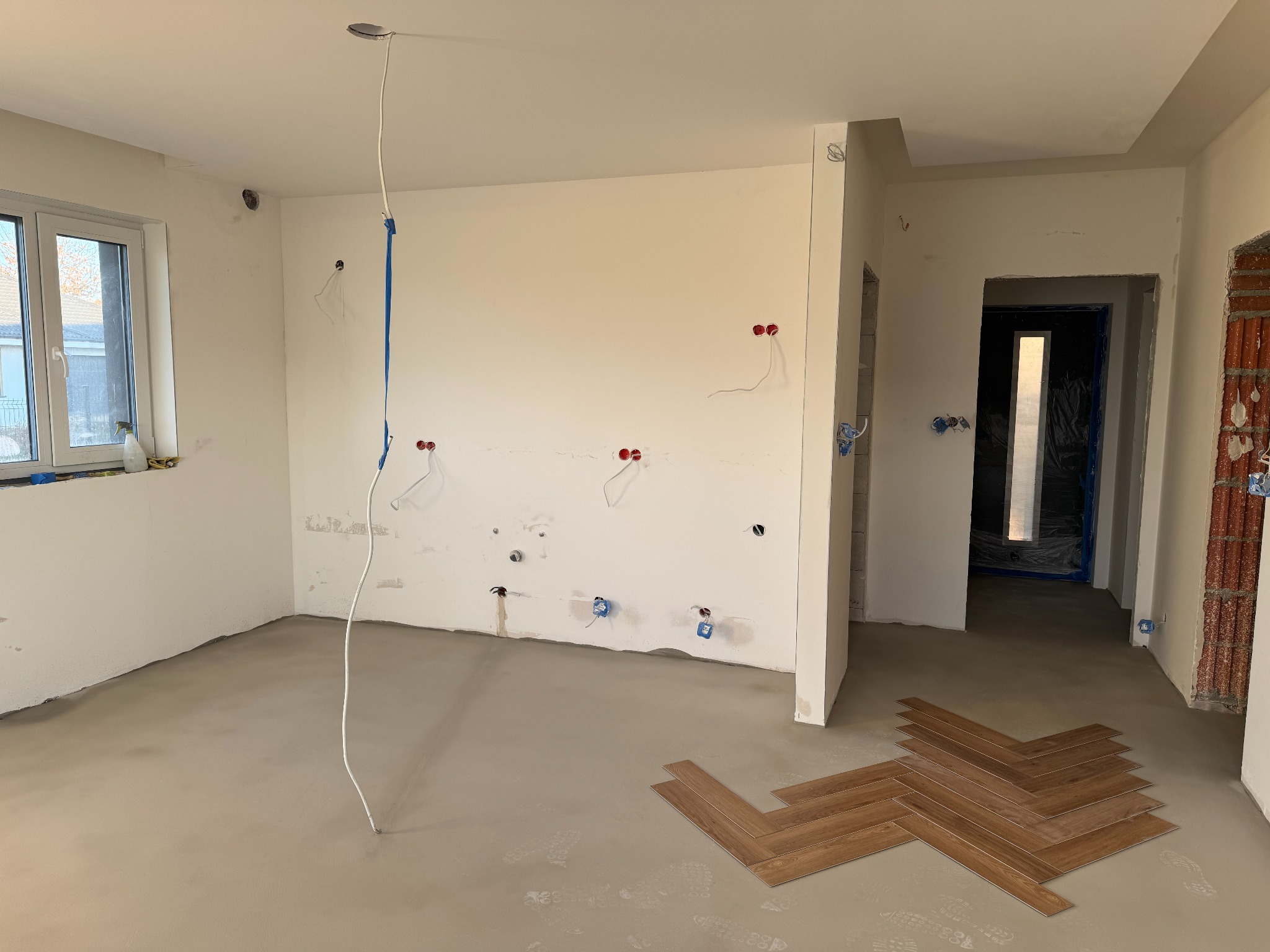 Wnętrze w trakcie prac wykończeniowych: wylewka, instalacja elektryczna, fragment ułożonych paneli w jodełkę. Widoczne przygotowania do dalszych prac.