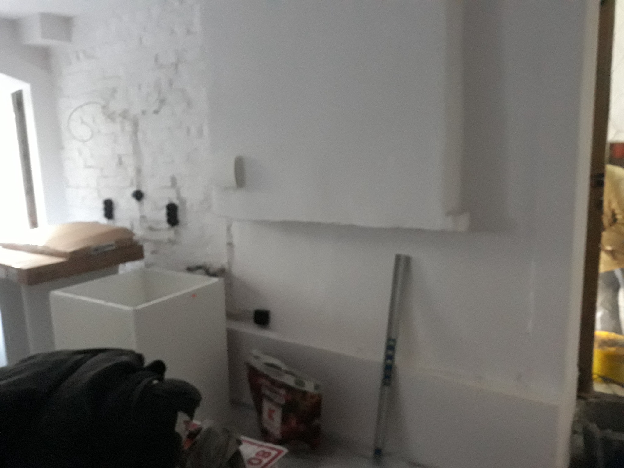 Świeżo otynkowana ściana z widocznymi śladami po instalacjach elektrycznych, biała cegła w tle, przygotowania do dalszych prac wykończeniowych.