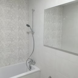 Rem Mod - Wykończona łazienka z wanną, chromowaną armaturą i lustrem, ściana wyłożona płytkami w odcieniach szarości i bieli.