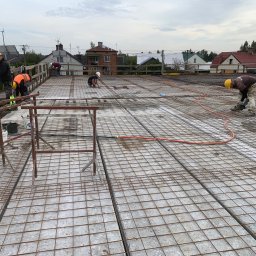 GREAT HOUSE Marcin Kobylarz - Zbrojenie stropu domu jednorodzinnego z widocznymi pracownikami w kaskach, przygotowującymi konstrukcję pod wylanie betonu. Widok z góry na plac budowy.