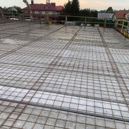 GREAT HOUSE Marcin Kobylarz - Siatka zbrojeniowa na stropie budynku w trakcie budowy, widok z góry. W tle zabudowa jednorodzinna i pochmurne niebo.