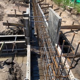 GREAT HOUSE Marcin Kobylarz - Zbrojenie w szalunku pod fundament, widoczni pracownicy w odblaskowych kamizelkach. Ujęcie z góry, ukazujące detale konstrukcji i przygotowania do zalewania betonem.