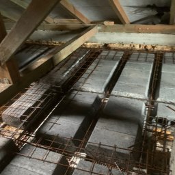 GREAT HOUSE Marcin Kobylarz - Zbrojenie stropu Teriva z betonowymi pustakami, widoczne drewniane elementy konstrukcji dachu i butelka wody. Ujęcie z góry, surowy stan budowy.