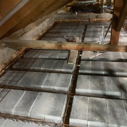 GREAT HOUSE Marcin Kobylarz - Zbrojenie pod wylewkę na poddaszu z widocznymi bloczkami betonowymi, siatką zbrojeniową i drewnianą konstrukcją dachu. W tle narzędzia i butelka wody.