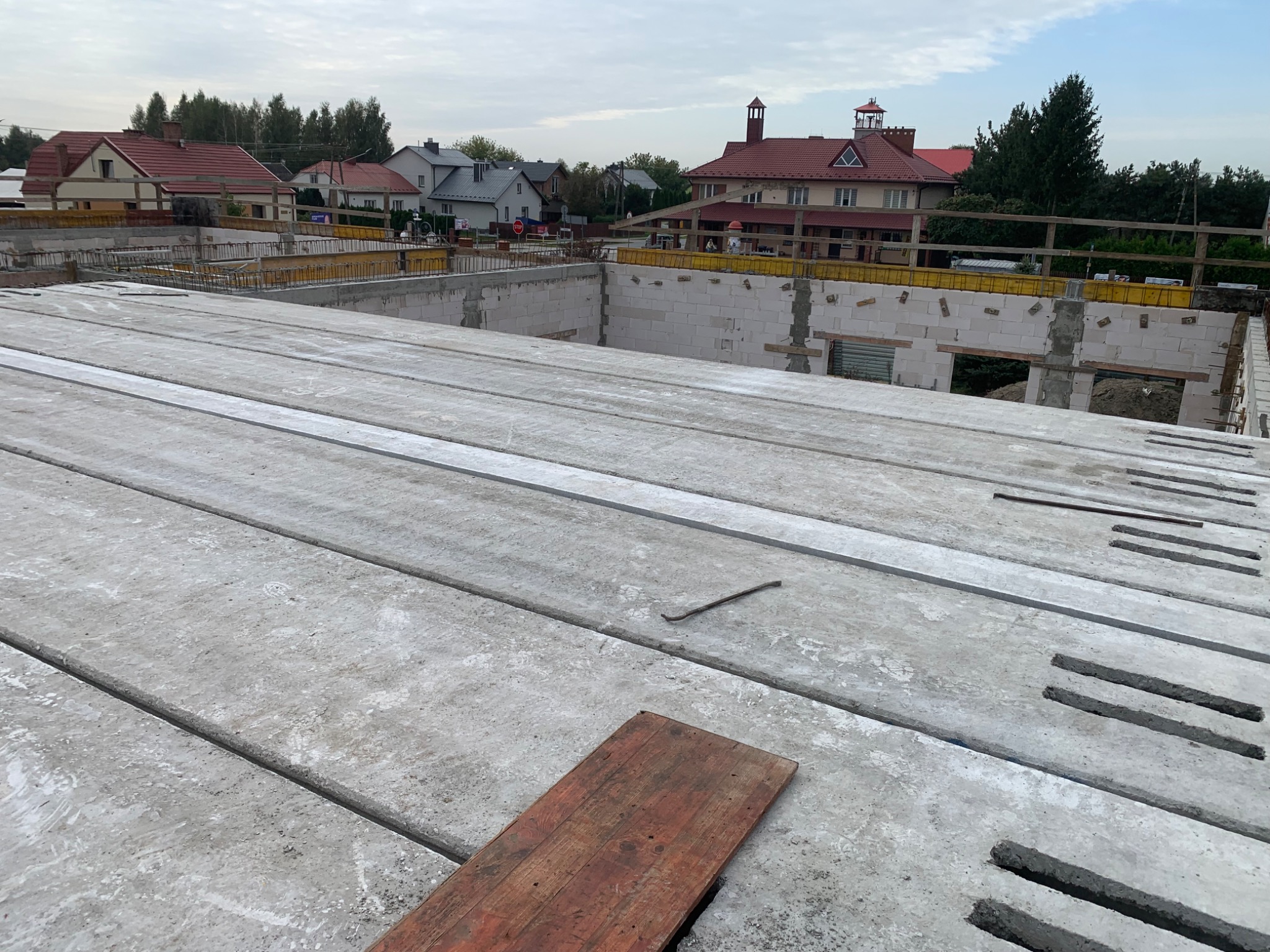 Betonowy strop Teriva z widocznymi belkami i pustakami, przygotowany do zalania betonem. W tle budynki mieszkalne i pochmurne niebo.