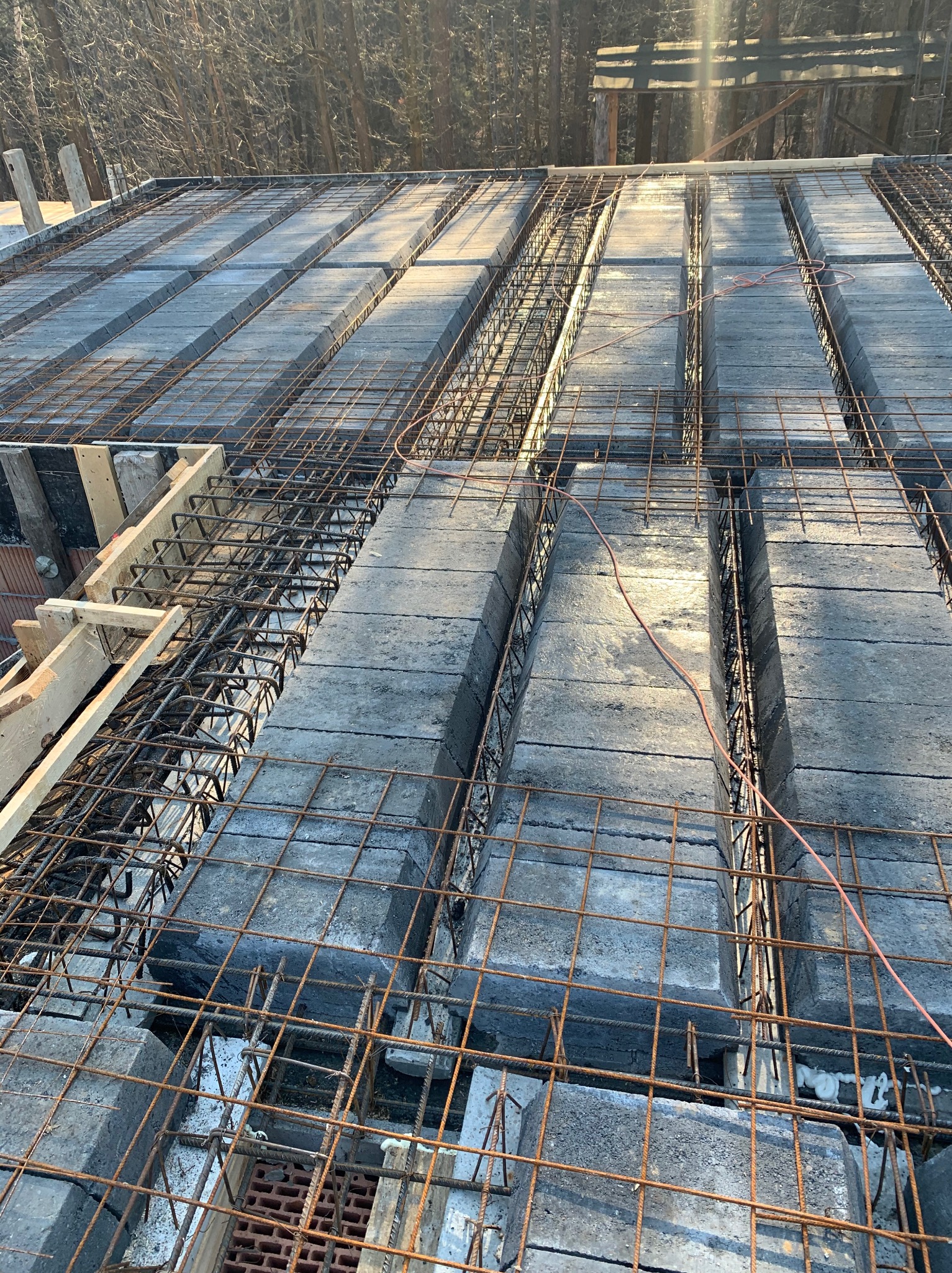 Zbrojenie stropu Teriva z betonowymi pustakami, widoczne pręty zbrojeniowe i drewniane szalunki. Słoneczne oświetlenie podkreśla strukturę betonu.