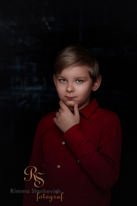 Portret młodego chłopca w czerwonej koszuli, z dłonią pod brodą, na ciemnym tle z subtelnymi wzorami.