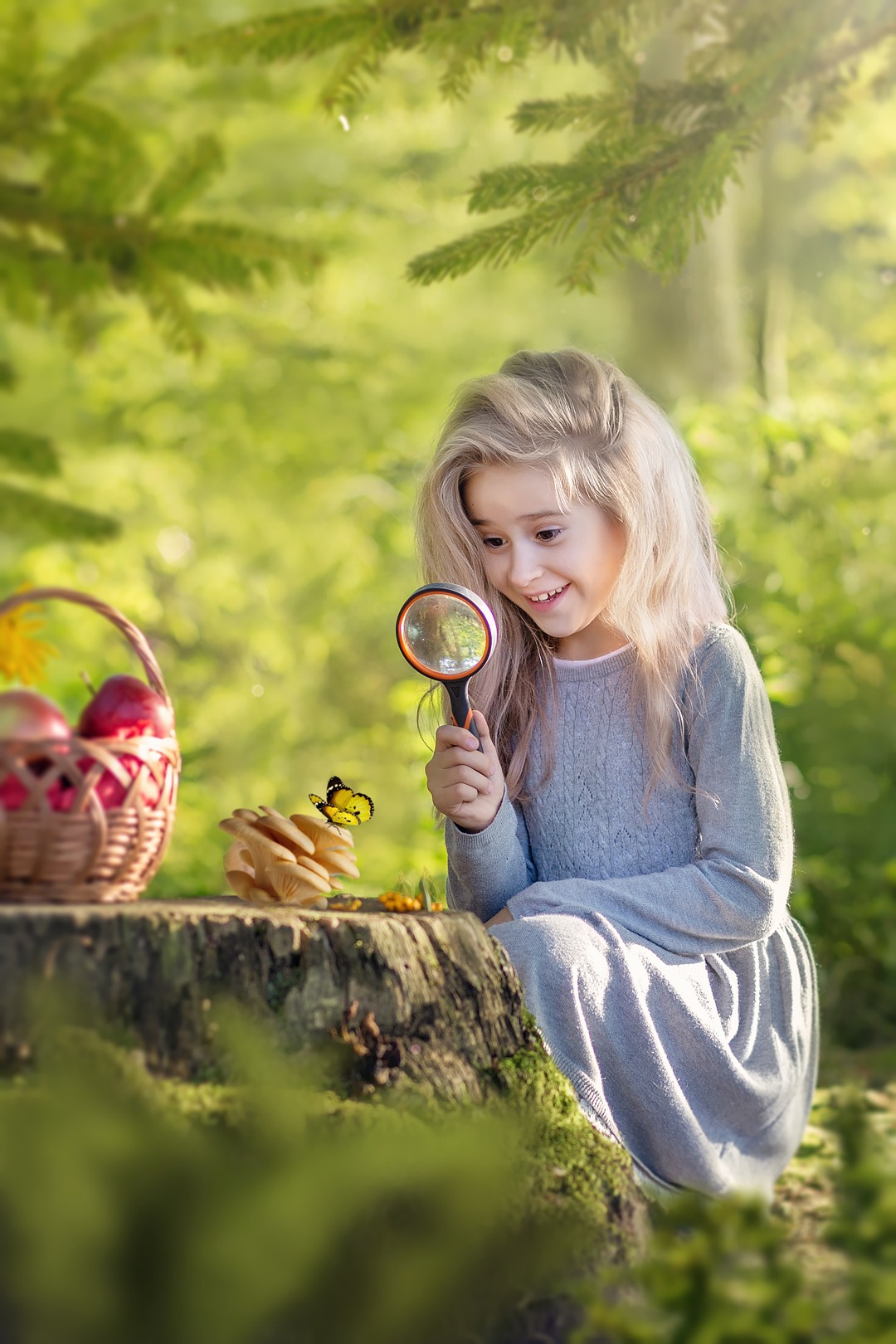 Dziewczynka z blond włosami przygląda się motylowi przez lupę na tle leśnej scenerii, obok koszyk z jabłkami.