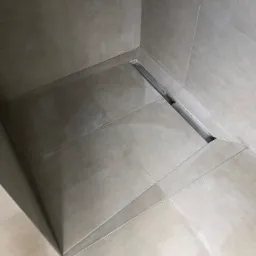 Beżowe płytki podłogowe i ścienne w kabinie prysznicowej z odpływem liniowym ze stali nierdzewnej.