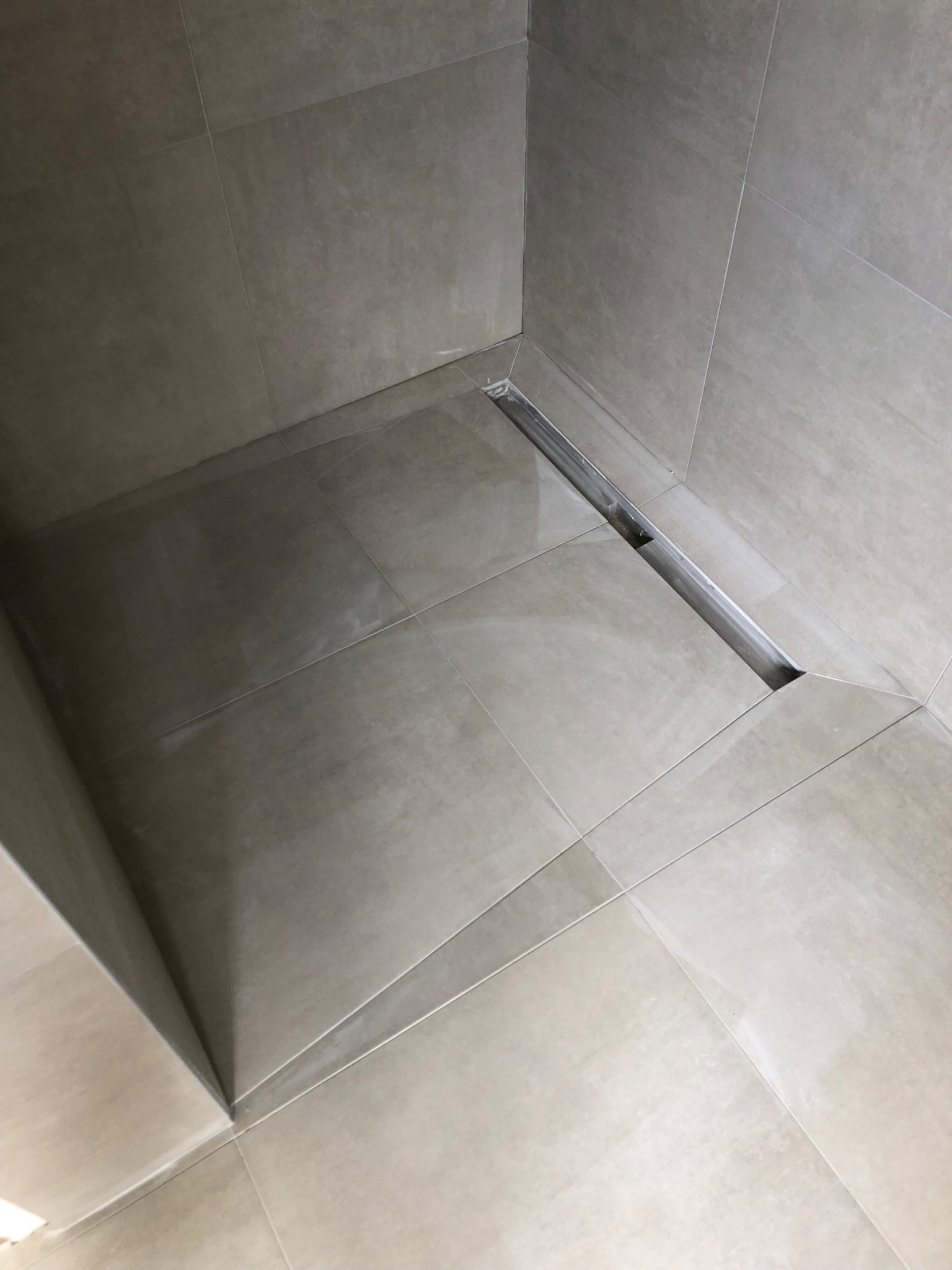 Beżowe płytki podłogowe i ścienne w kabinie prysznicowej z odpływem liniowym ze stali nierdzewnej.