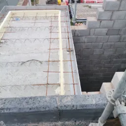 Wzmocniona konstrukcja betonowa stropu z izolacją obwodową ze styropianu, widok z g&oacute;ry na placu budowy, z rusztowaniem i ułożonymi bloczkami betonowymi.