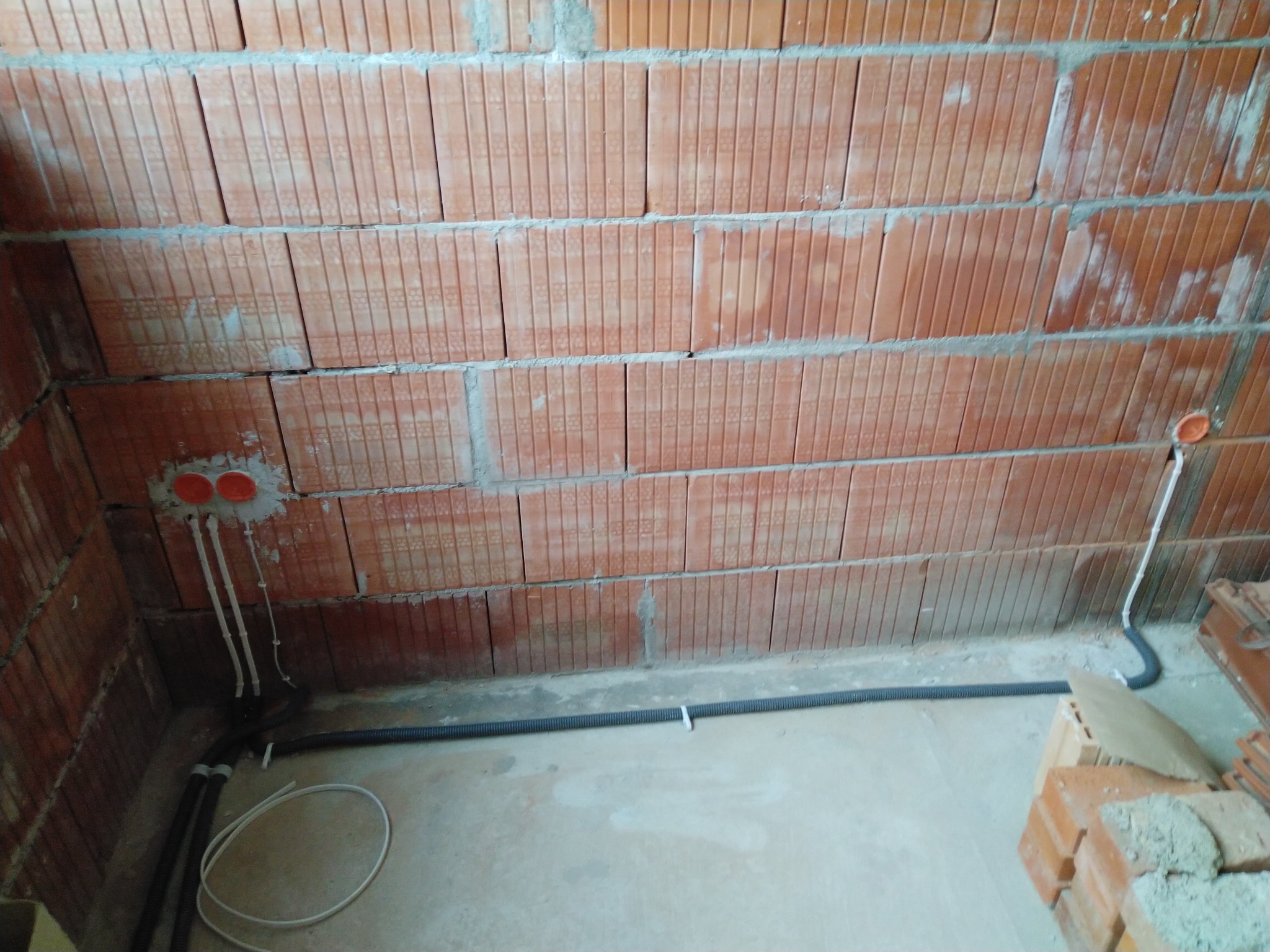 Wewnętrzna instalacja elektryczna w trakcie montażu w budynku z cegły dziurawki, widoczne kable w peszlu mocowane do podłoża opaskami, puszki instalacyjne w ścianie oraz przewody wyprowadzone...