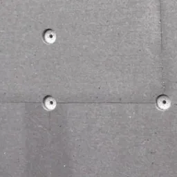 Szara ściana z widocznymi płytami izolacyjnymi i plastikowymi kołkami mocującymi, widoczne łączenia płyt.