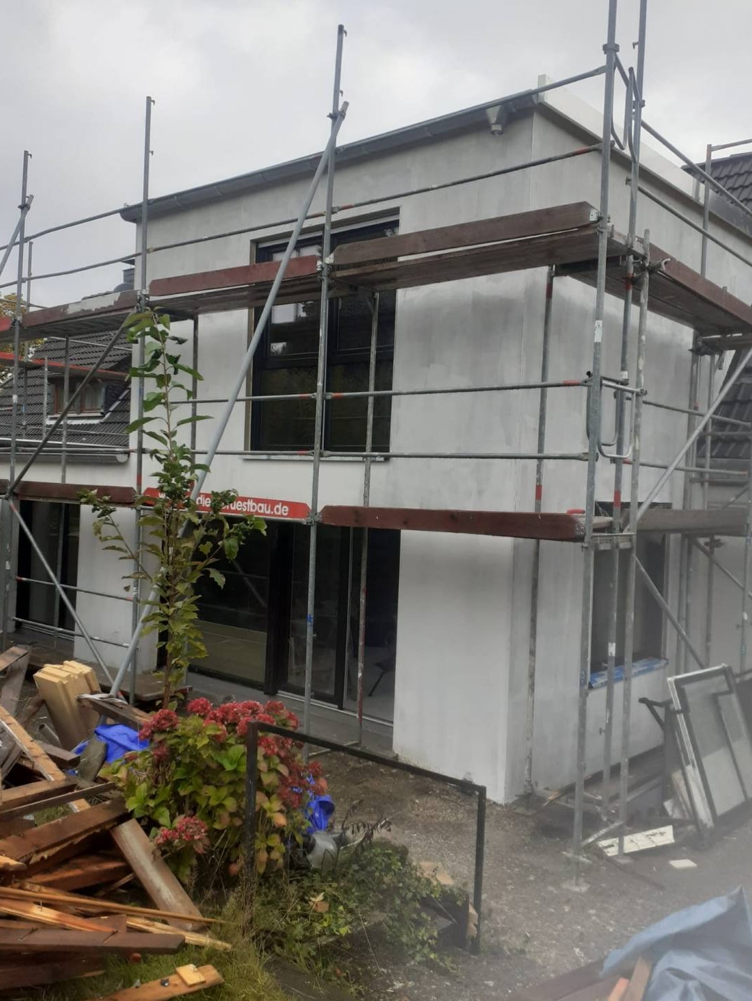 Dom w Bytomiu w trakcie prac elewacyjnych, na rusztowaniu, surowy tynk, widoczne okna i drzwi, teren wokół domu częściowo zagospodarowany.