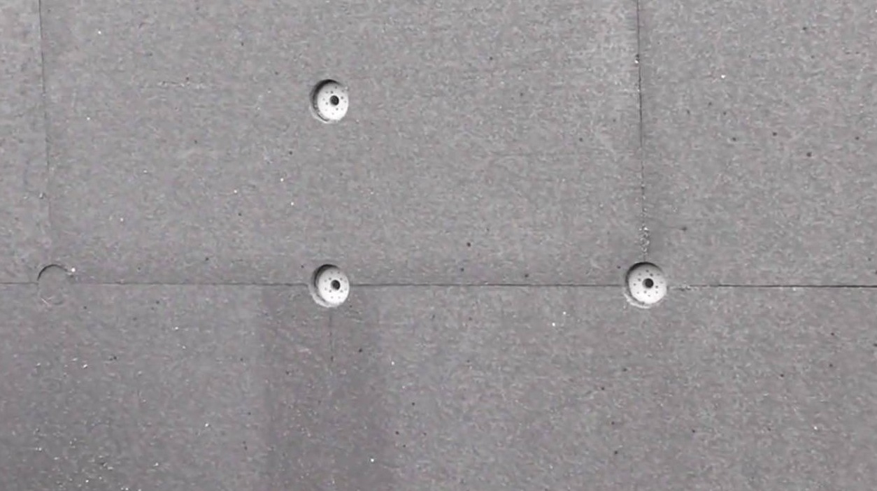 Szara ściana z widocznymi płytami izolacyjnymi i plastikowymi kołkami mocującymi, widoczne łączenia płyt.