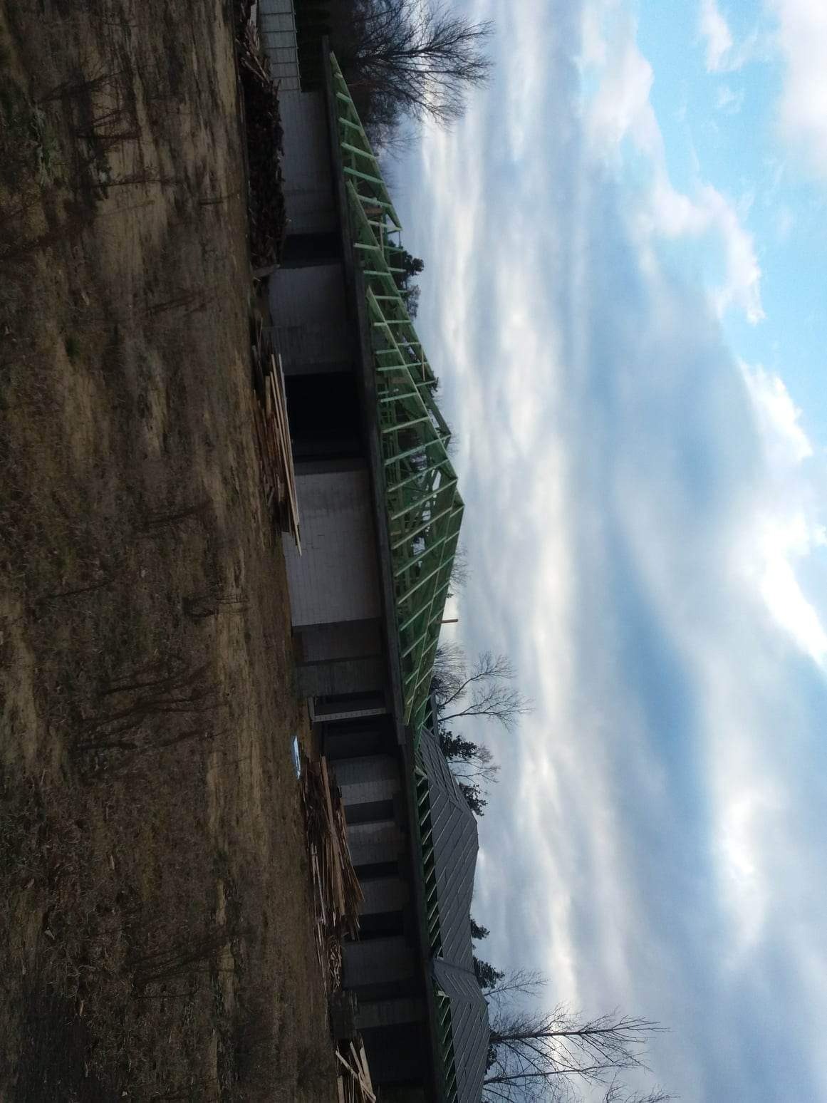 Budowa domu jednorodzinnego z widoczną drewnianą konstrukcją dachu w trakcie montażu, na tle pochmurnego nieba.