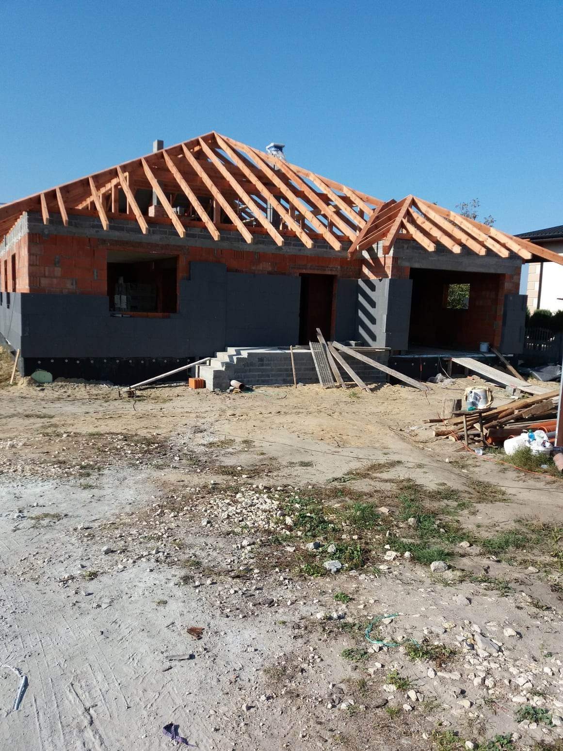 Wznoszenie konstrukcji drewnianej dachu na domu w Myszkowie, widoczna więźba dachowa w trakcie montażu, ściany z pustaków i ocieplenie fundamentów.