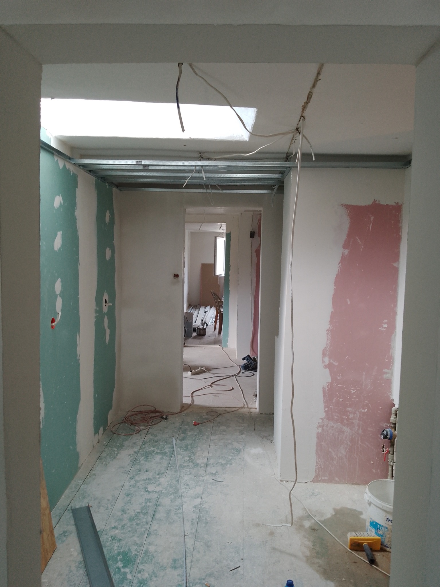 Wnętrze w trakcie prac wykończeniowych: widoczne profile sufitowe, częściowo położona płyta gipsowo-kartonowa na ścianach z widocznymi otworami na instalacje, przewody elektryczne zwisające...