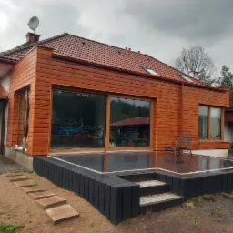 Dom jednorodzinny z drewnianą elewacją i ciemnym tarasem, widok z ogrodu w pochmurny dzień.