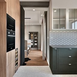 Asilé Privé Design - Wizualizacja kuchni z drewnianą zabudową, piekarnikiem i szafkami w kolorze butelkowej zieleni oraz heksagonalnymi płytkami na ścianie. W tle widoczny salon z jadalnią.