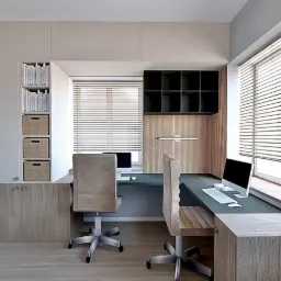 Nowoczesne biuro domowe z dwoma stanowiskami pracy, jasnymi biurkami z drewnianymi frontami, roletami w oknach i wbudowanymi półkami z koszami na dokumenty.