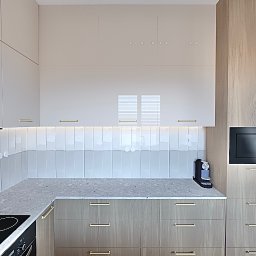 Asilé Privé Design - Nowoczesna kuchnia z białymi i drewnianymi szafkami, złotymi uchwytami, płytkami wertykalnymi i czarną kuchenką mikrofalową Amica.