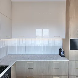 Nowoczesna kuchnia z białymi i drewnianymi szafkami, złotymi uchwytami, płytkami wertykalnymi i czarną kuchenką mikrofalową Amica.