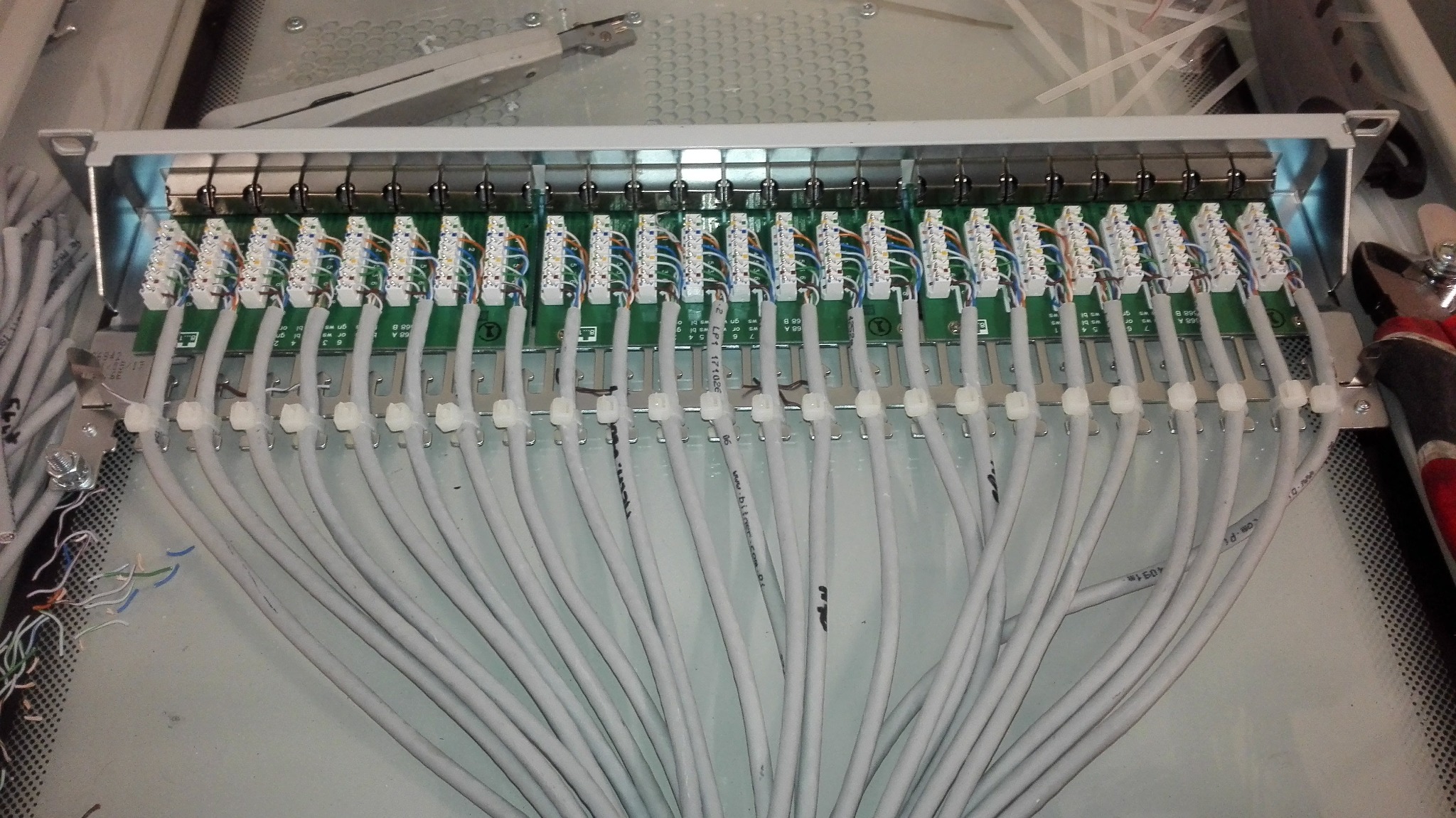 Panel krosowniczy z podłączonymi kablami sieciowymi, widoczne narzędzia instalacyjne