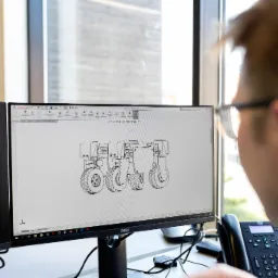 Inżynier w okularach pracuje nad projektem ciągnika rolniczego w programie SolidWorks na podwójnym monitorze, widoczne okno z rysunkiem technicznym 3D.