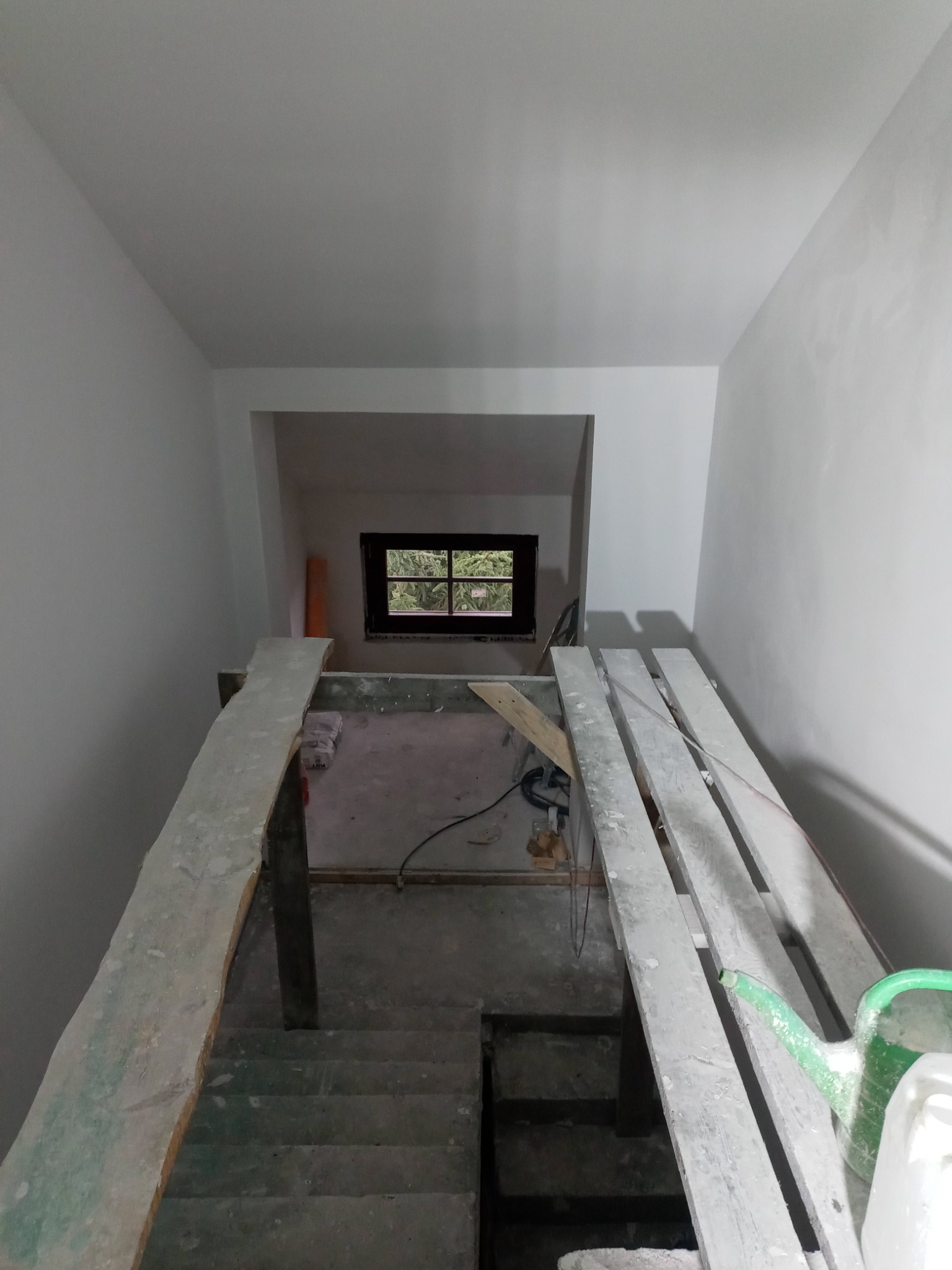 Wnętrze w trakcie malowania: widok na schody i okno z rusztowania, ściany świeżo pomalowane na biało, widoczne narzędzia malarskie.