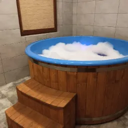 Drewniana beczka kąpielowa z niebieskim wnętrzem wypełniona pianą, z drewnianymi schodkami, ustawiona w pomieszczeniu z szarymi płytkami.