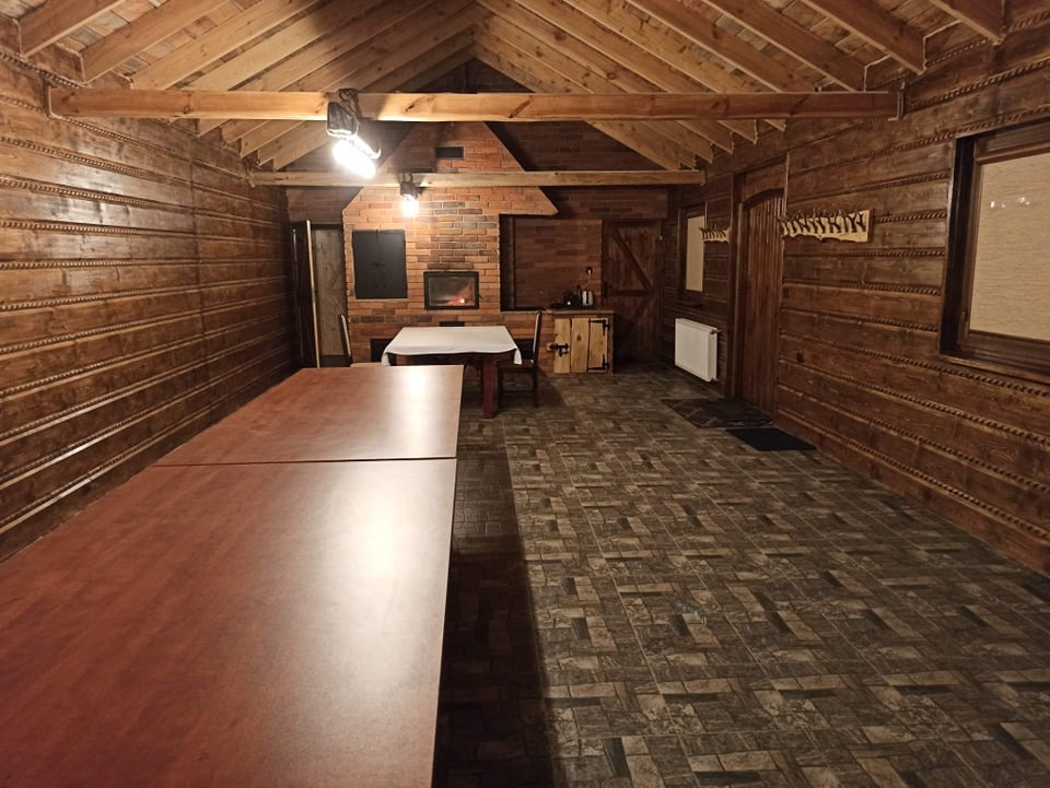 Wnętrze drewnianej sali z długim stołem i kominkiem z cegły, przygotowanej do organizacji wydarzenia.
