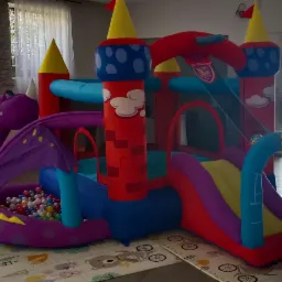 Kolorowy dmuchany zamek ze zjeżdżalnią i basenem z kulkami w kształcie smoka, ustawiony na podłodze w jasnym pomieszczeniu.