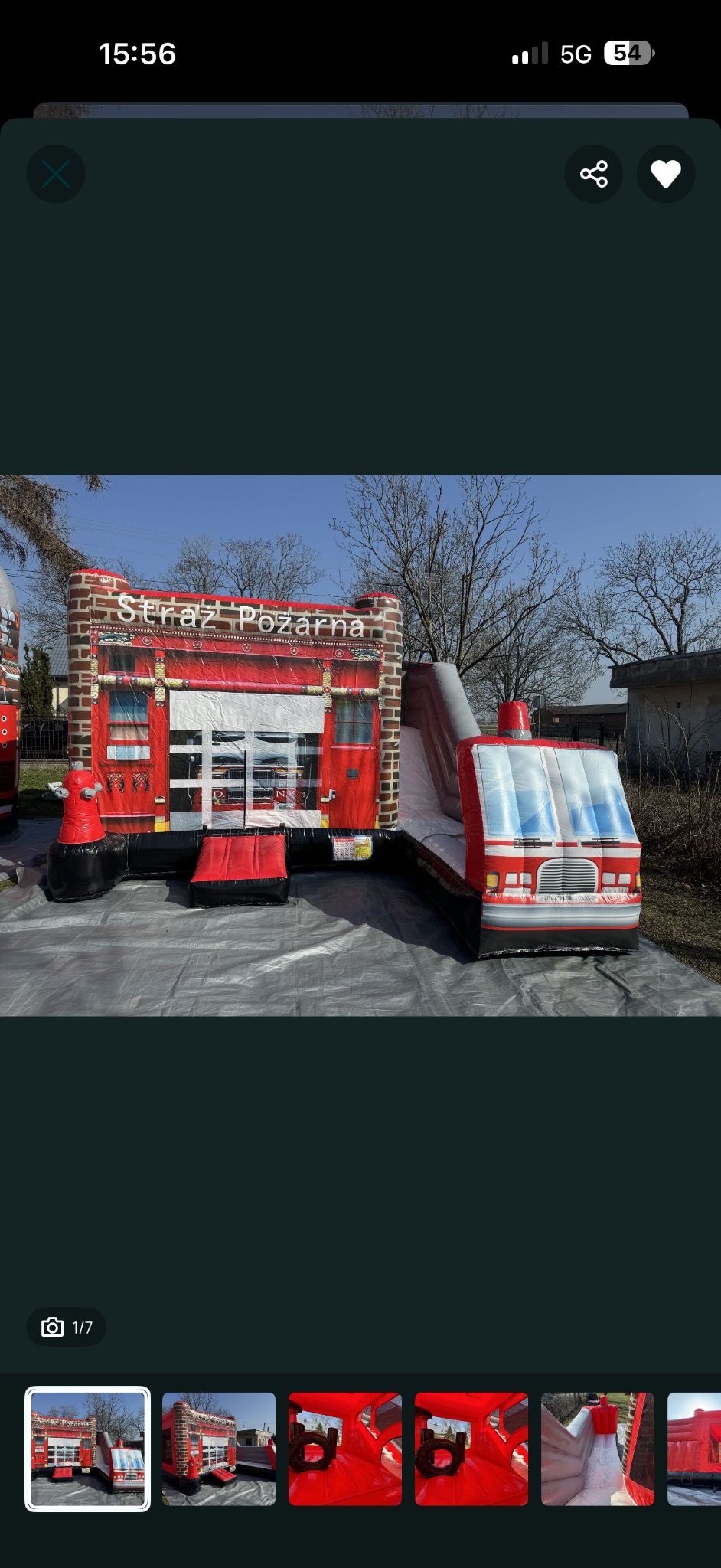 Dmuchany zamek w kształcie wozu strażackiego z napisem 'Straż Pożarna', ustawiony na szarej plandece, z widoczną zjeżdżalnią i elementami imitującymi wóz strażacki.