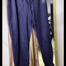 Tekstylowe love - Granatowe spodnie dresowe marki Converse z widocznym logo na nogawce, wiszące na czarnym wieszaku na tle lustra i beżowej zasłony.