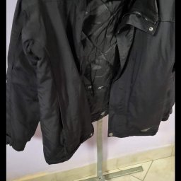 Tekstylowe love - Czarna kurtka sportowa marki 4F, wisząca na metalowym stojaku z wieszakiem, widoczna podszewka z logo marki.