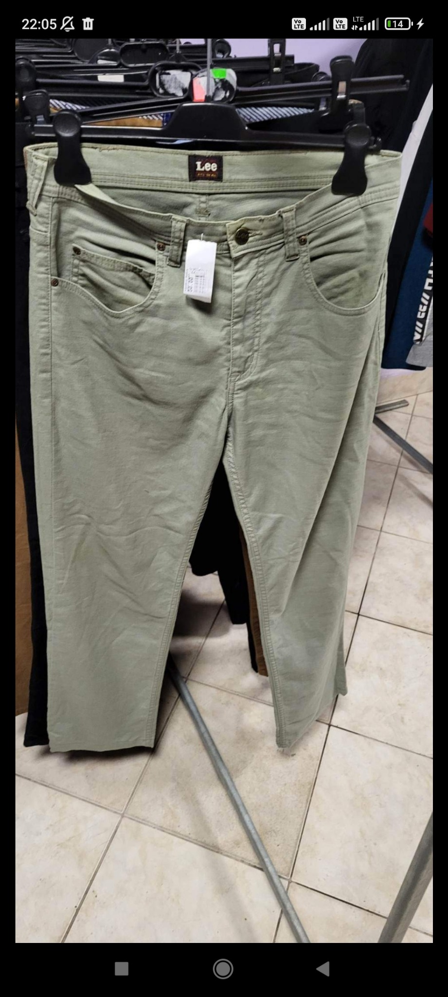 Jasnozielone spodnie marki Lee zawieszone na czarnym wieszaku z widoczną metką cenową, prezentowane w sklepie z odzieżą używaną.