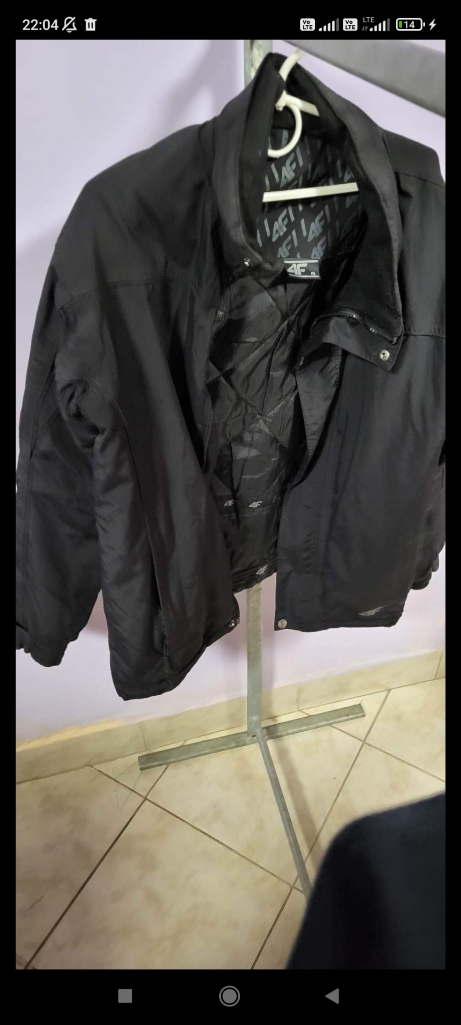Czarna kurtka sportowa marki 4F, wisząca na metalowym stojaku z wieszakiem, widoczna podszewka z logo marki.