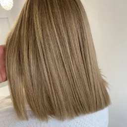 Tył głowy z prostą fryzurą w odcieniach blondu, delikatne refleksy, włosy do ramion, widoczny fragment białego swetra.