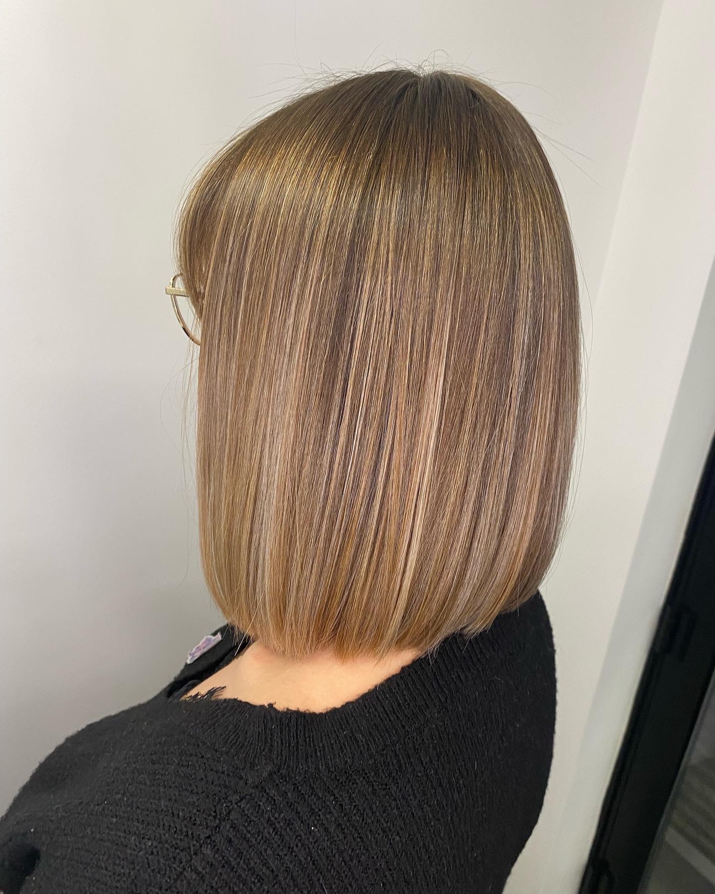 Włosy blond z refleksami, świeżo po strzyżeniu na boba, widoczne z tyłu, z delikatnym zaokrągleniem przy karku i okularami na uszach.