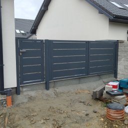 OGROBUD - Nowoczesne, poziome przęsła ogrodzeniowe z szarego metalu, zamontowane na betonowej podmurówce. Widoczne narzędzia i materiały budowlane. Tło stanowi ściana budynku.