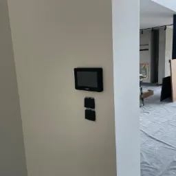 Panel sterowania alarmem i dwa gniazdka elektryczne zamontowane na ścianie w nowym domu w trakcie wykończenia, podłoga zabezpieczona folią malarską.