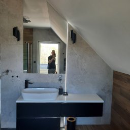 Dryju Design - Nowoczesna łazienka na poddaszu z umywalką nablatową, czarną szafką pod umywalką, szarą płytką imitującą kamień, oświetleniem LED i lustrem, w którym odbija się osoba robiąca zdjęcie.