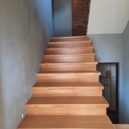 Dryju Design - Drewniane schody z dębowymi stopniami na betonowej posadzce, ściana z cegły w tle, szare ściany, minimalistyczny design.