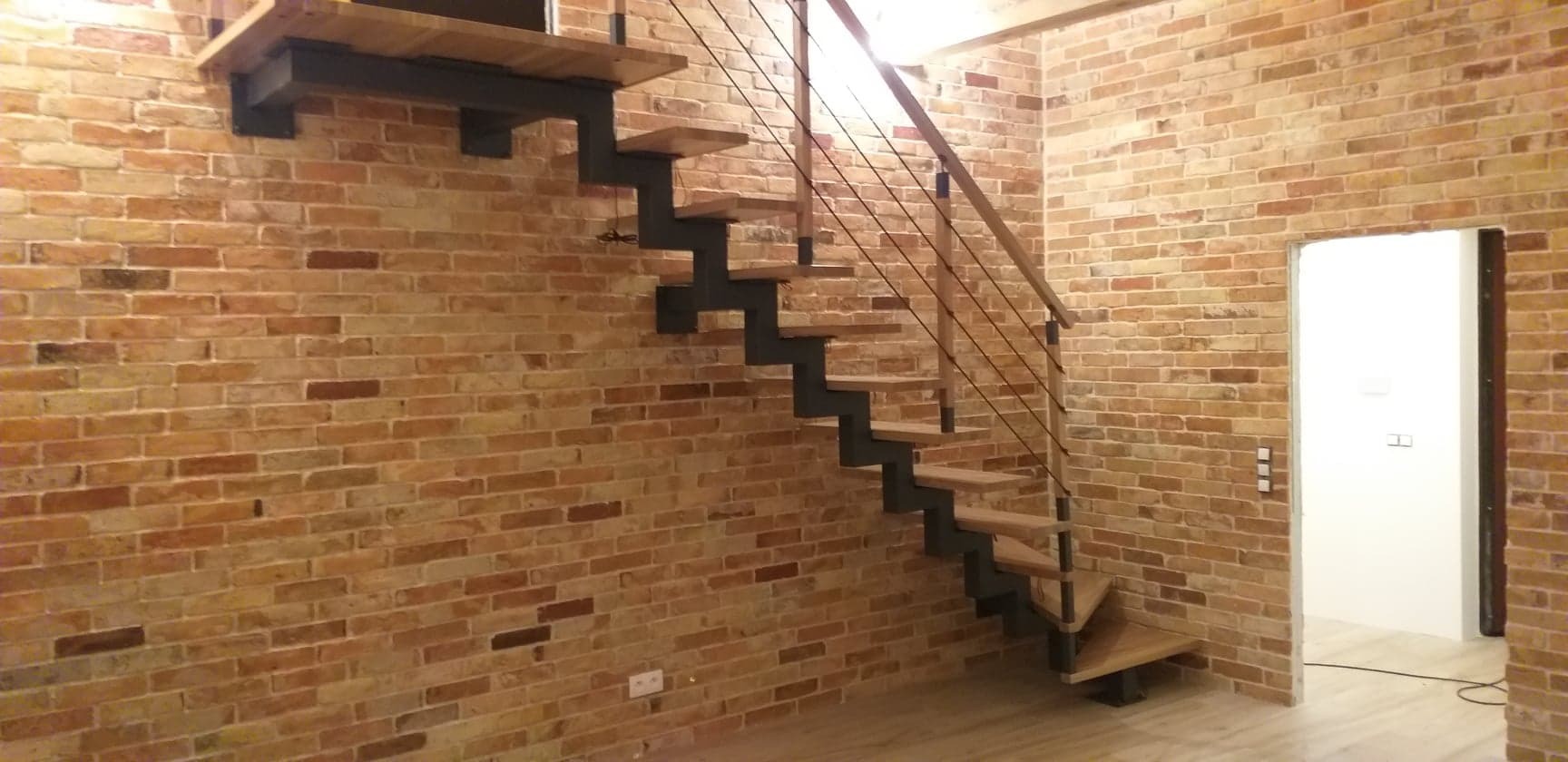 Schody drewniane z metalowymi elementami w stylu loftowym na tle ceglanej ściany w Kalwarii Zebrzydowskiej.
