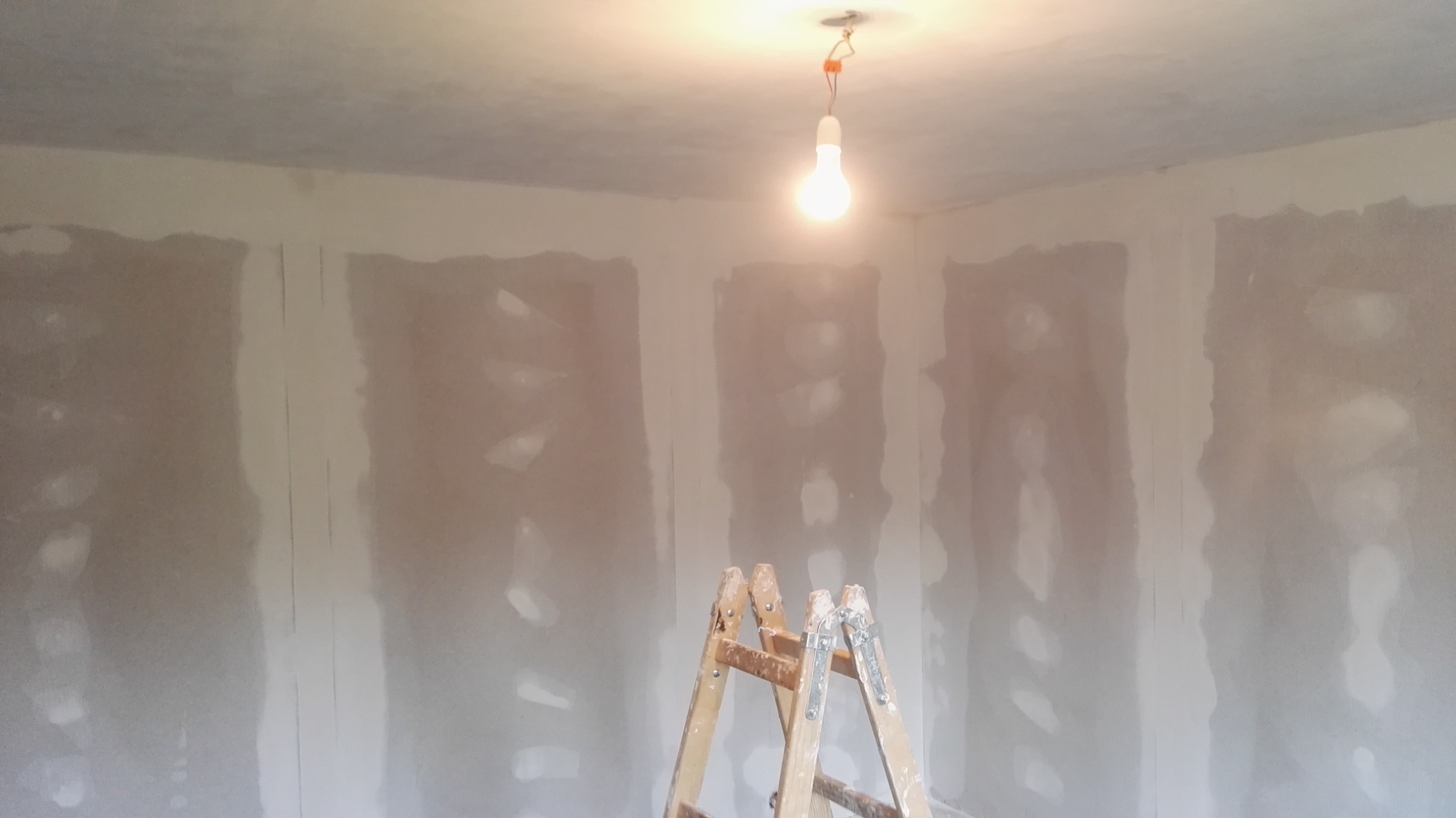 Pokój w trakcie szpachlowania ścian płytami gipsowo-kartonowymi, widoczna drabina malarska i wisząca żarówka.
