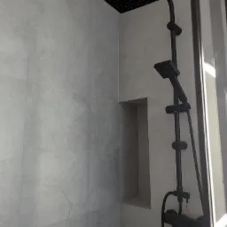 Nowoczesna kabina prysznicowa z czarną armaturą i wnęką w szarej, imitującej kamień, płytce. Minimalistyczny design z wyraźnym kontrastem kolorystycznym.