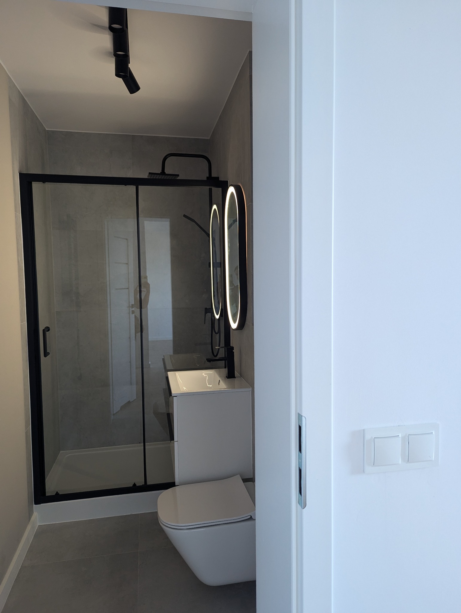 Nowoczesna łazienka z kabiną prysznicową, umywalką i toaletą w Lutomiersku. Czarna armatura i oświetlenie punktowe podkreślają minimalistyczny design.